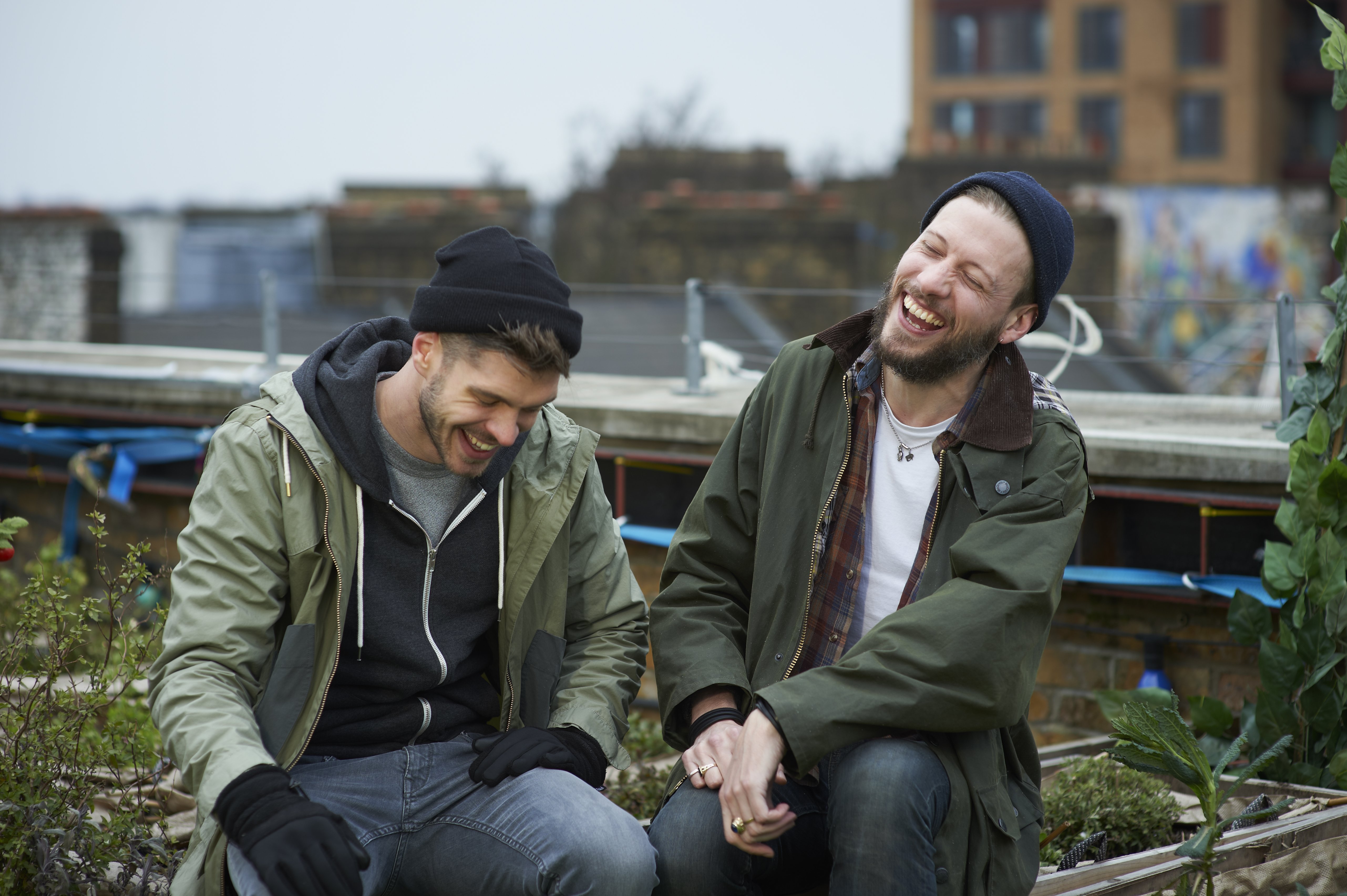 Two young men are pictured sitting among plants in an allotment on an urban roof garden sharing a joke | Source: Getty Images