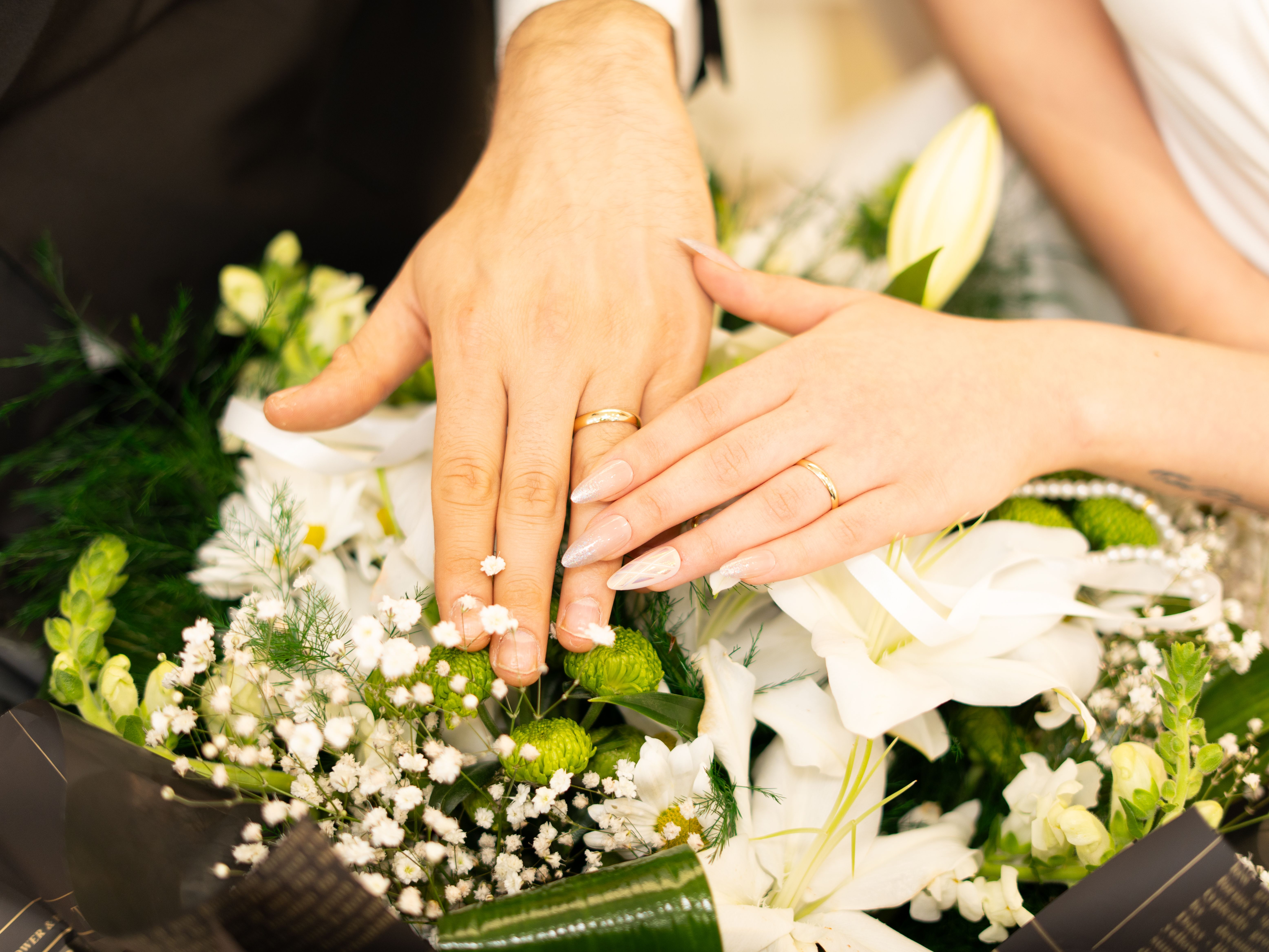 Close-up of hands wearing wedding rings resting on a bouquet of flowers | Source: Pexels