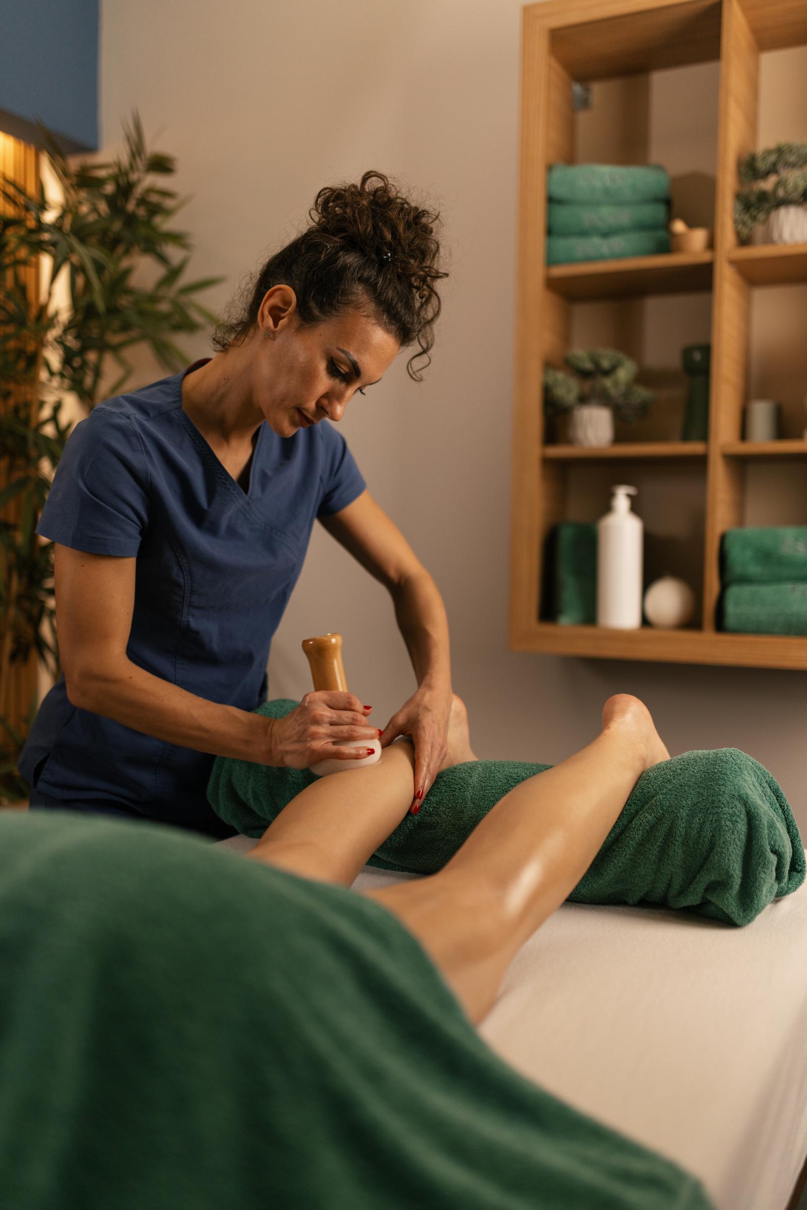 A woman administering a gua sha massage on a client's legs | Source: Getty Images