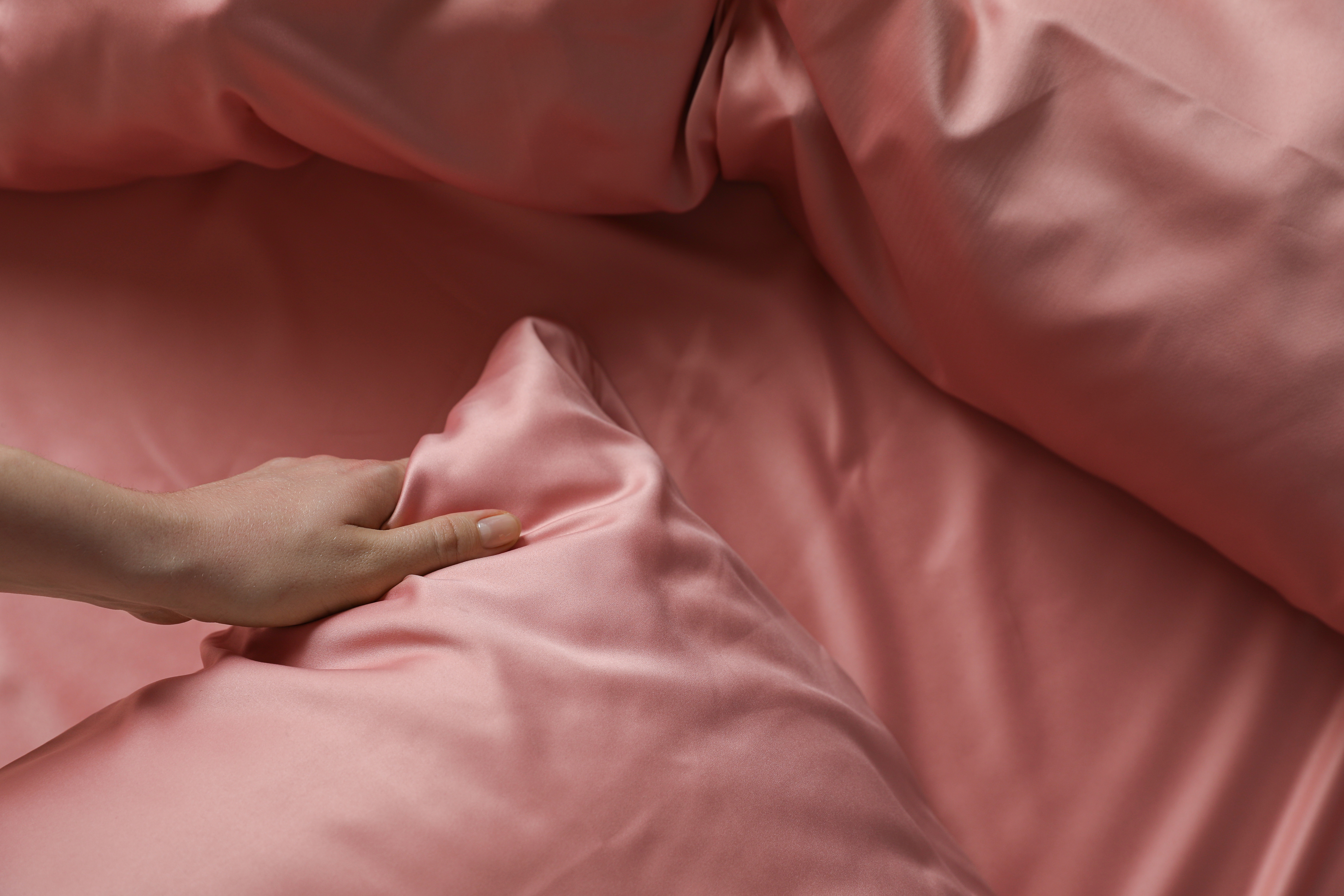 A woman makes up a bed with luxurious pink linen. | Source Getty Images