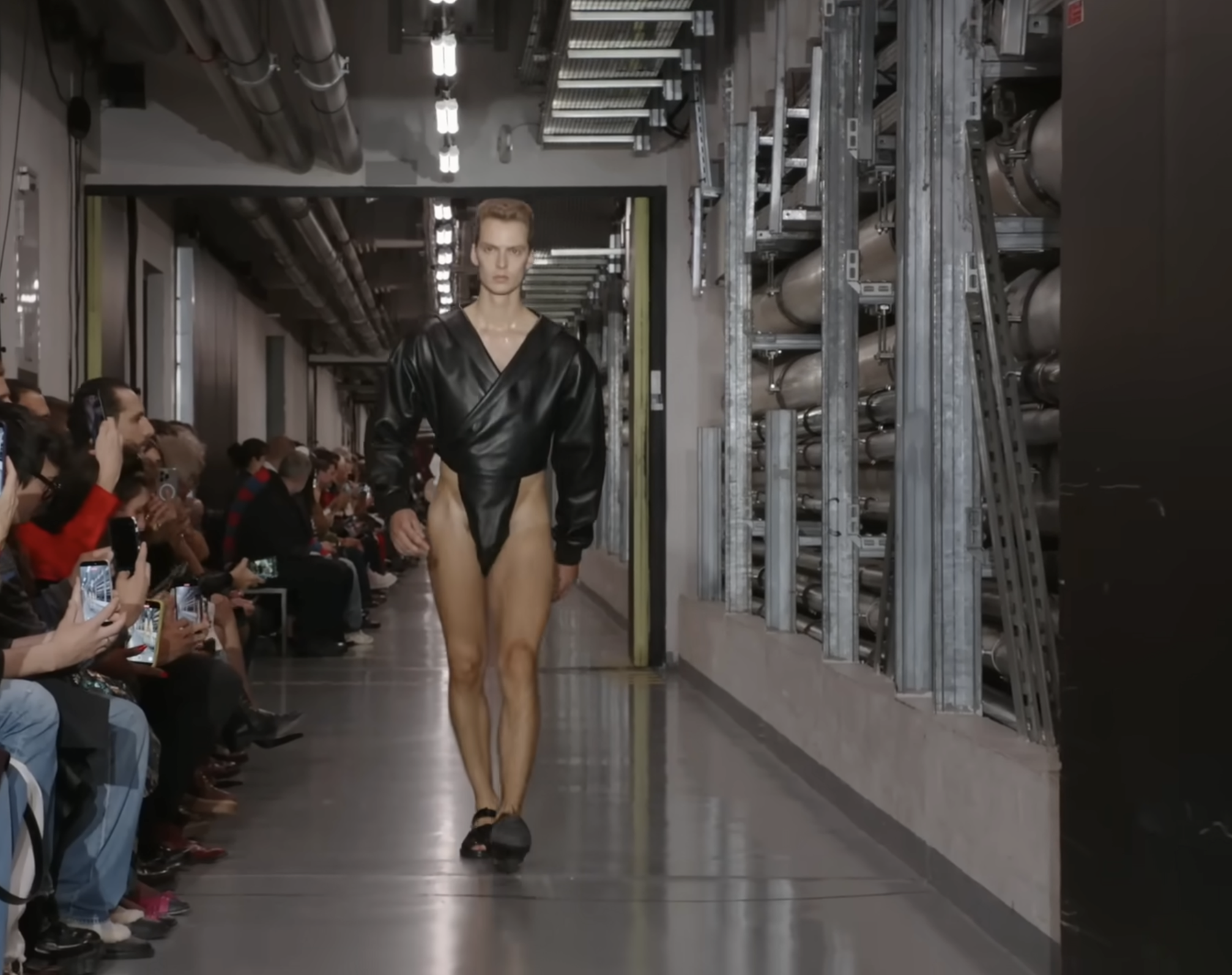 Then came futuristic bodysuits cut high on the leg. This model wears a black version with a voluminous, inflated design that highlights his toned legs — a distinctive take on the bodysuit, tailored to the male physique. From a post dated October 5, 2025. Source: Youtube/@jeanpaulgaultier