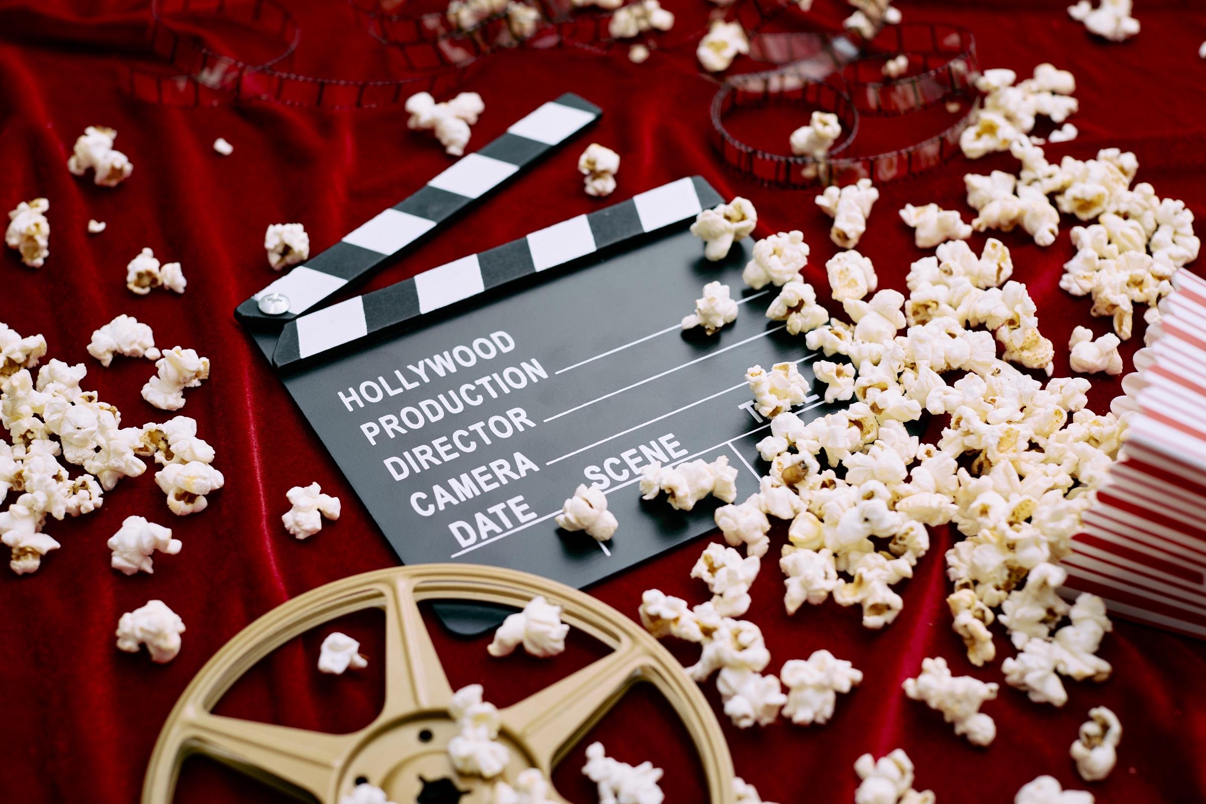 A clapperboard, film reel, film and spilled popcorn on a red satin background | Source: Getty Images