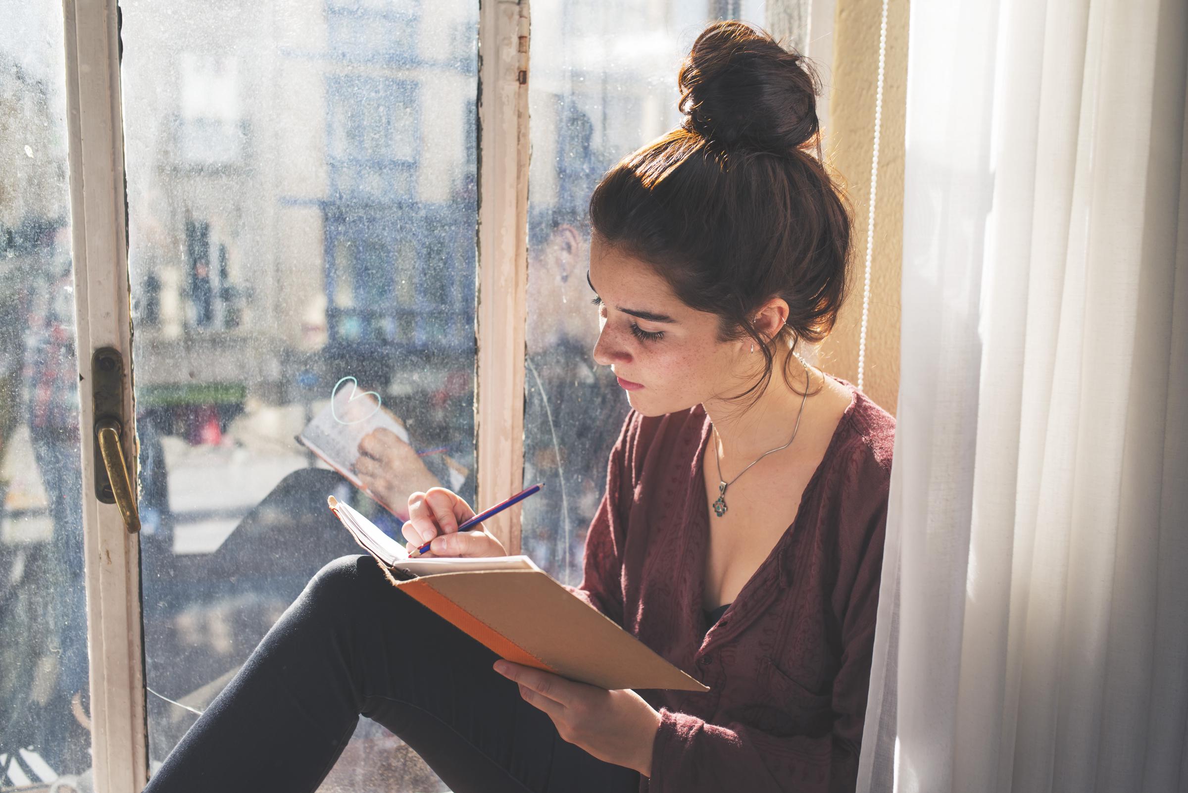 A woman writes in her notebook by a window | Source: Getty Images