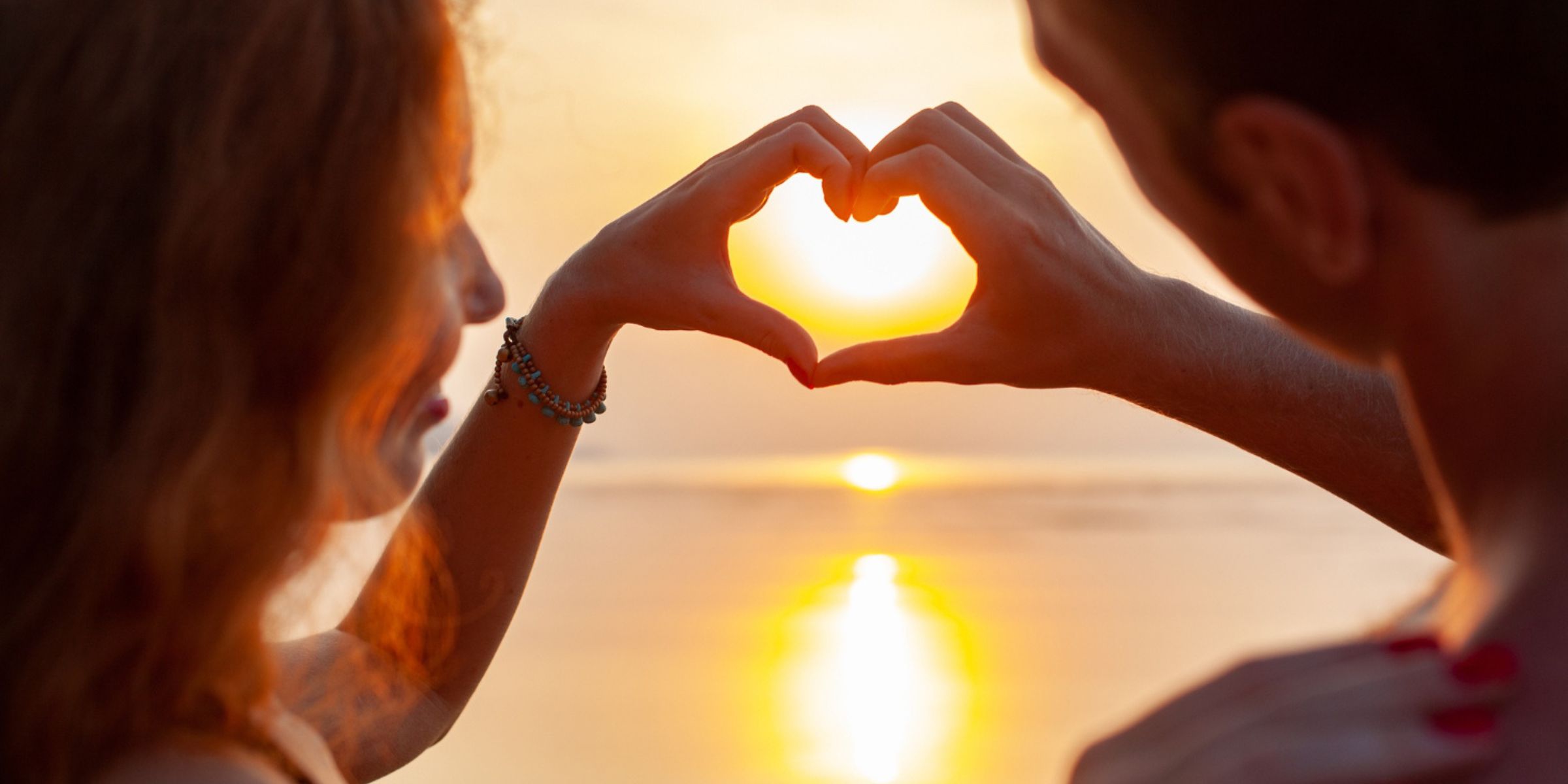 A couple forming a heart shape with their hands while watching the sunset | Source: Magnific