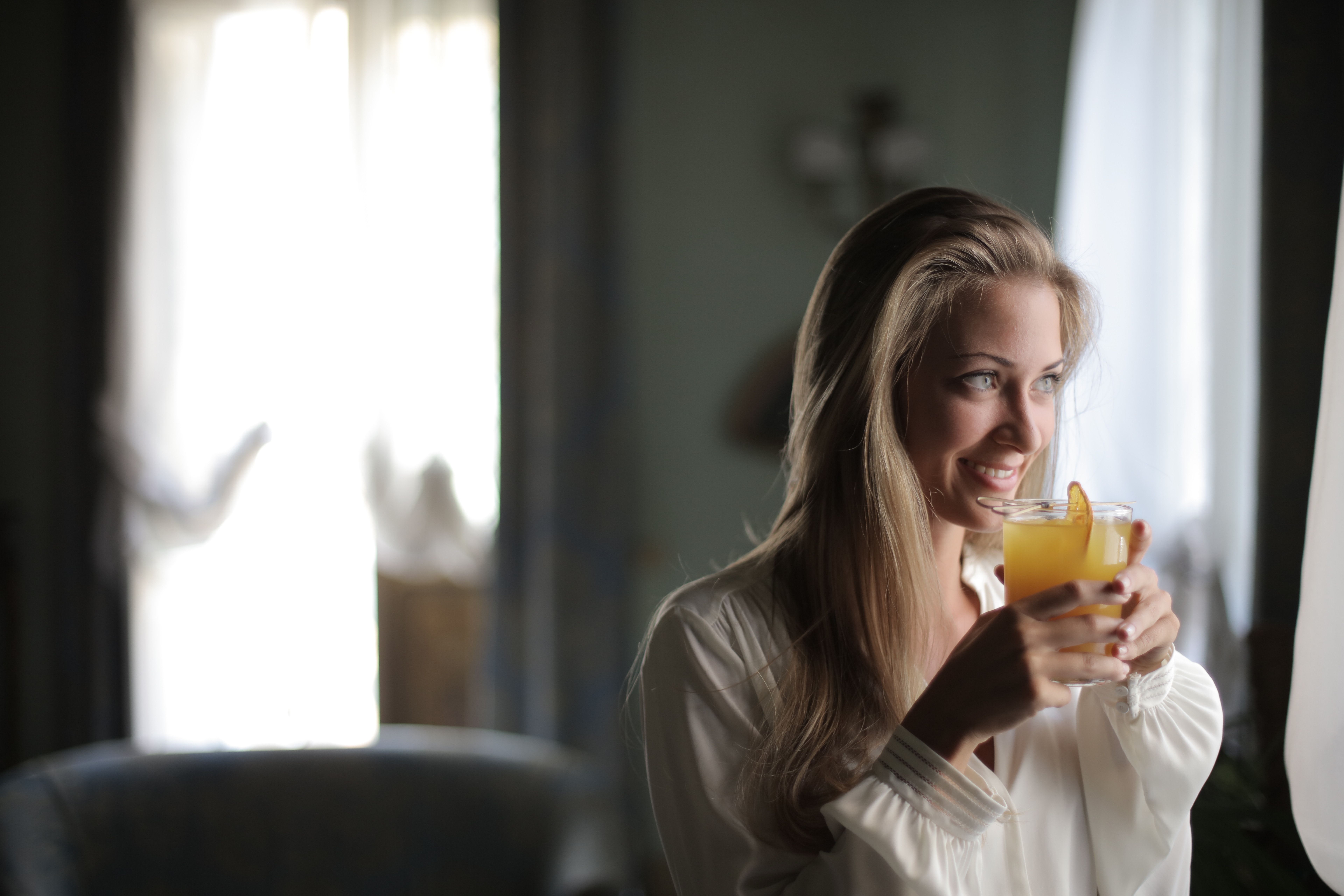 A woman holding a cocktail while staring out the window | Source: Pexels