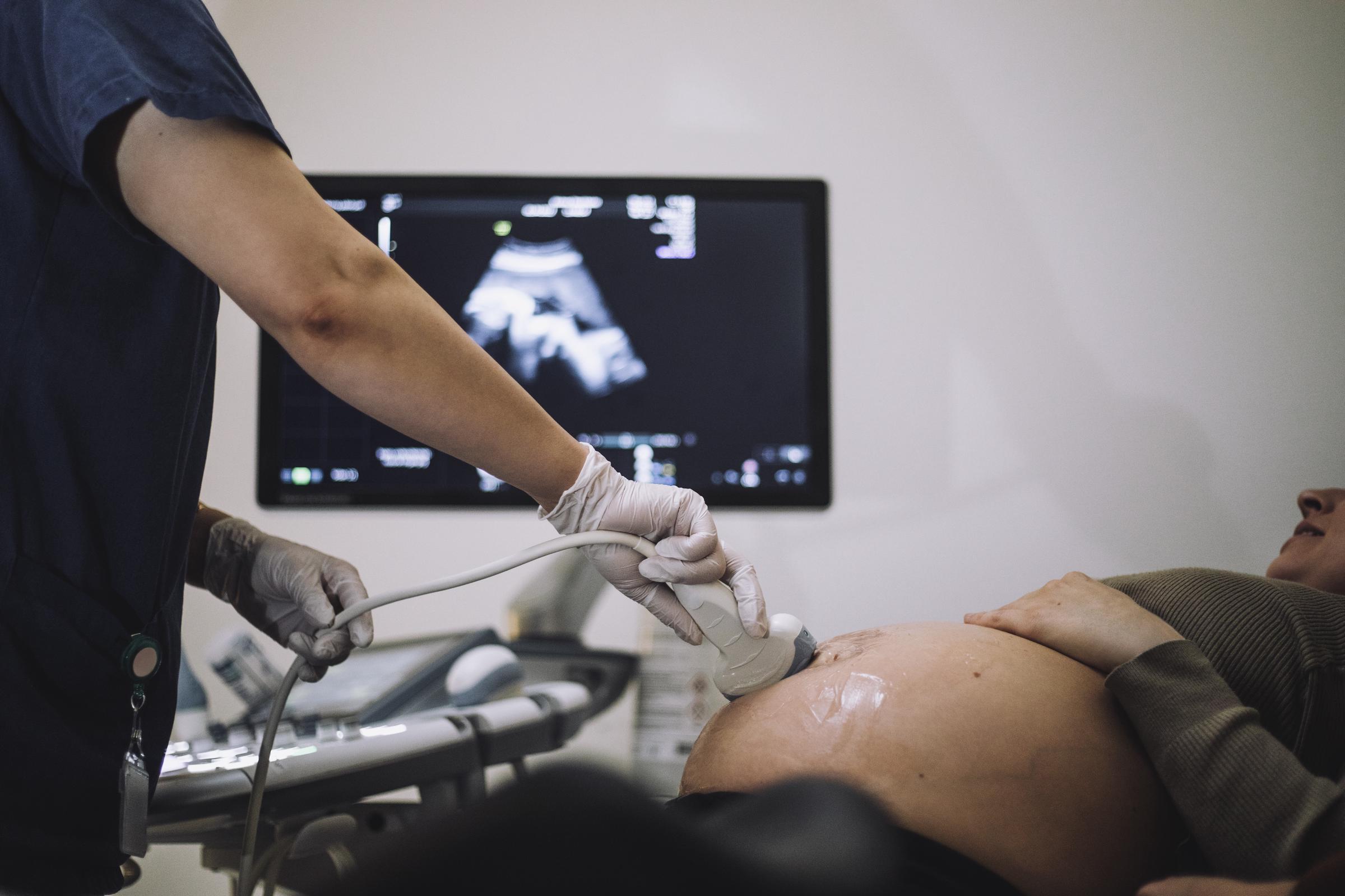 A gynaecologist performing an ultrasound on a pregnant woman's belly | Source: Getty Images