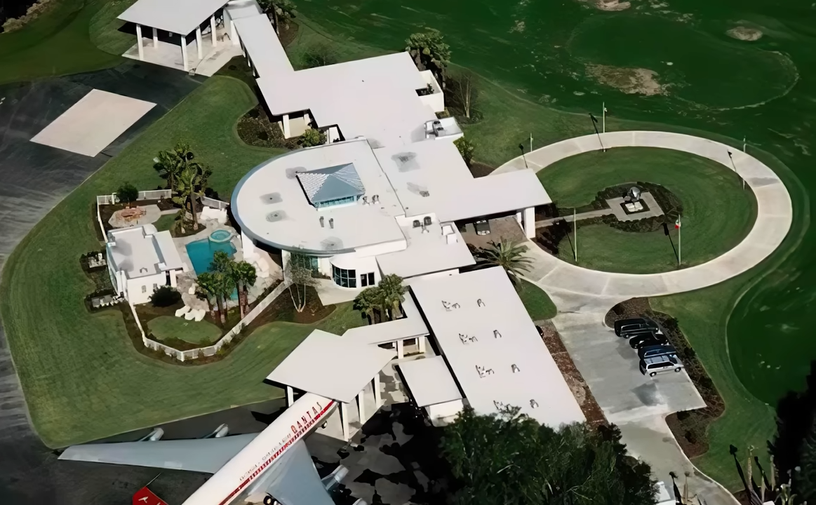 Travolta's aviation-focused property combines a curved modern residence, landscaped grounds, a pool, and space for a large aircraft. | Source: YouTube/@Therichest